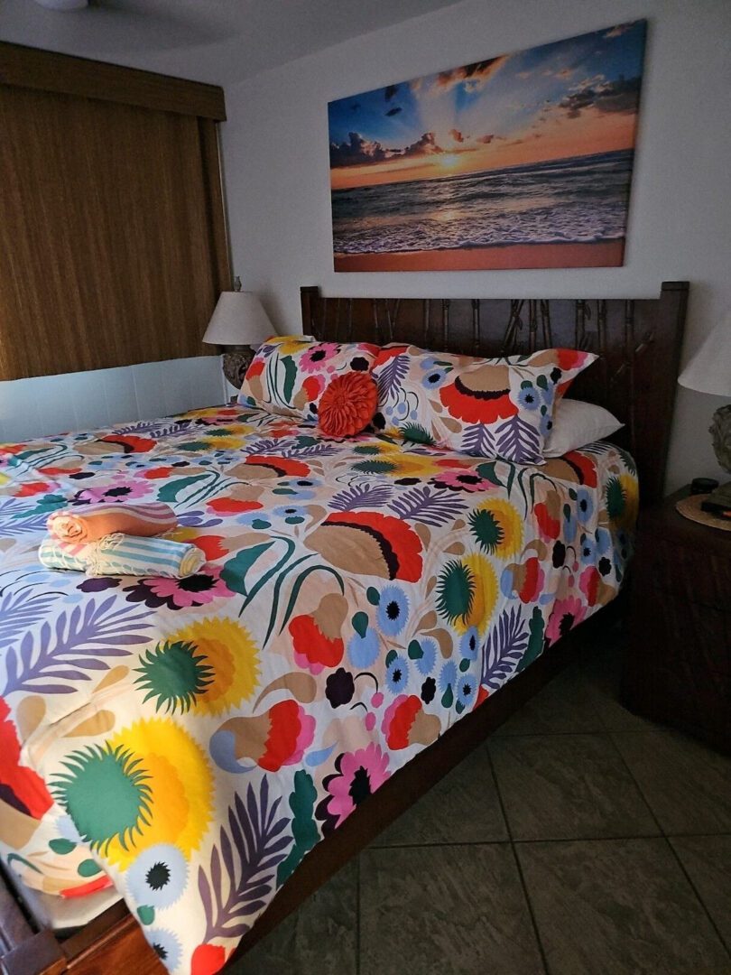 A bed with colorful sheets and pillows in front of a painting.