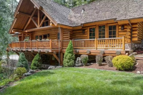 A large log cabin with a deck and lawn.