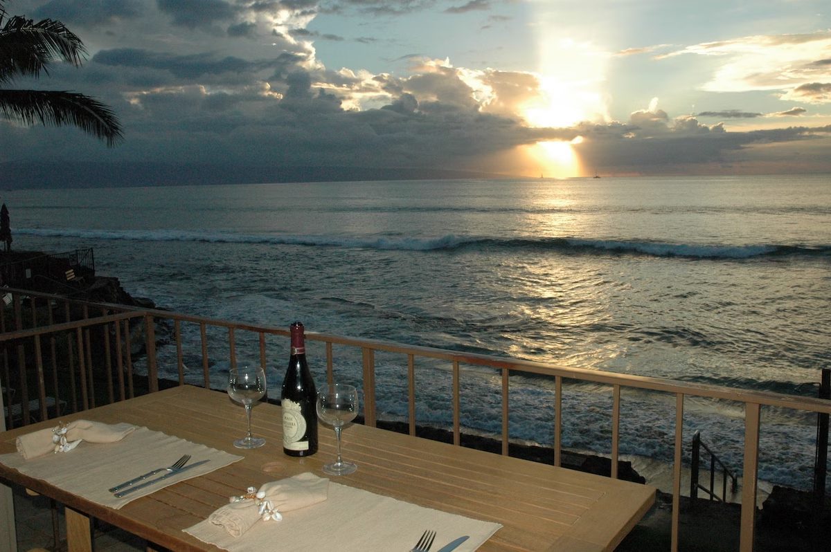 A table with wine and glasses on it near the ocean.