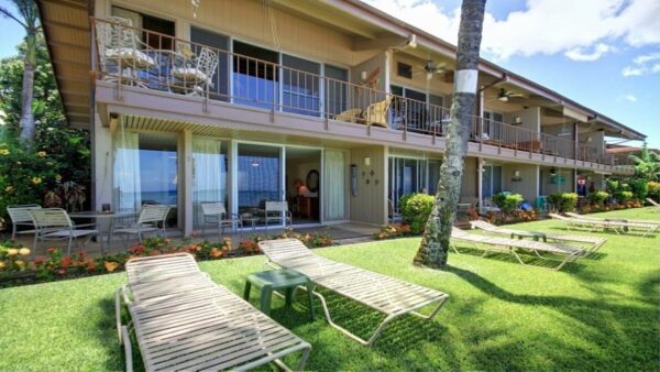 A lawn with chairs and tables in front of the ocean.