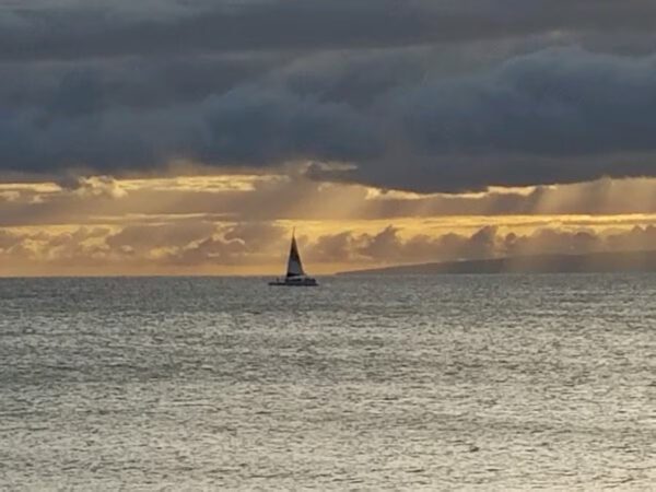 A sailboat is sailing in the ocean at sunset.