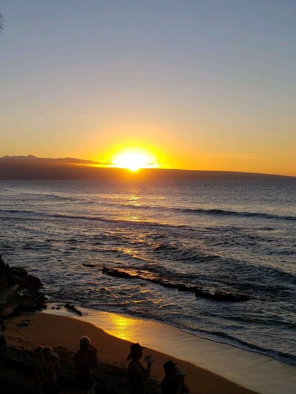 A sunset over the ocean with waves crashing on it.