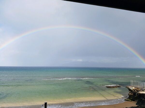 A rainbow over the ocean with a view of the beach.