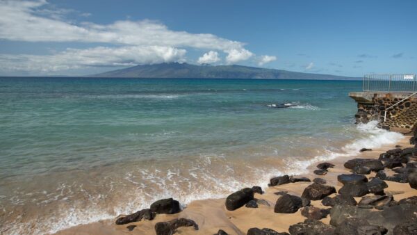 A beach with waves crashing on it and the ocean in the background.