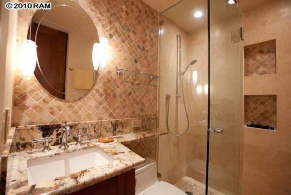 A bathroom with marble counter tops and a glass shower door.