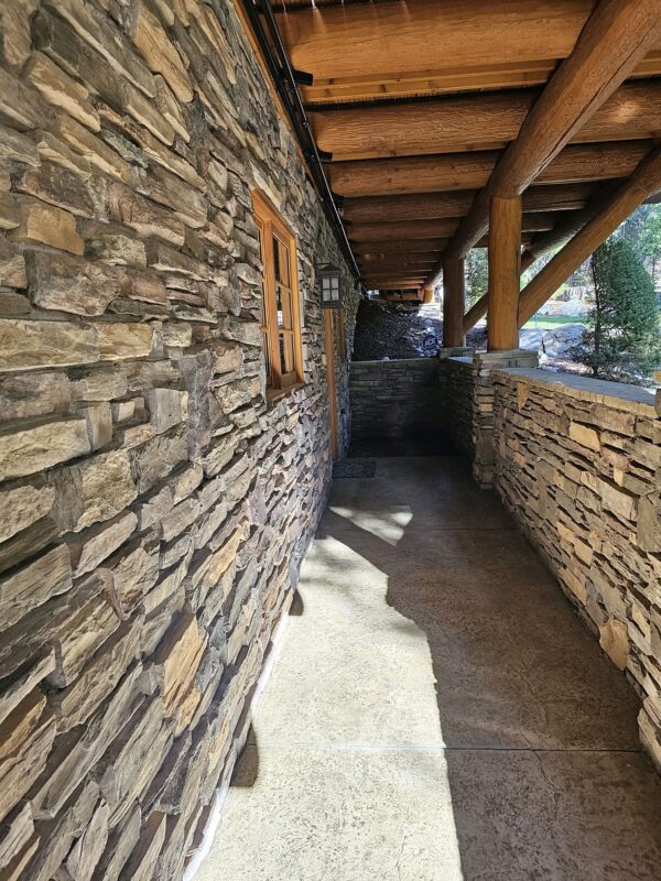 A stone wall with a wooden ceiling and a brick walkway.